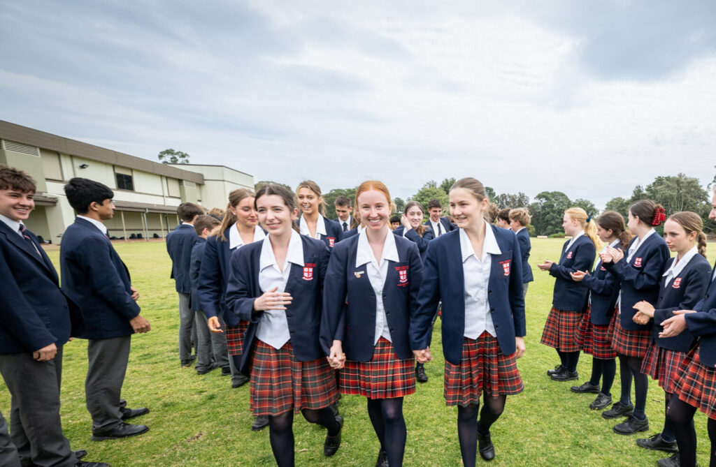 Three female Northholm Grammar senior students walking outdoors surrounded by other students